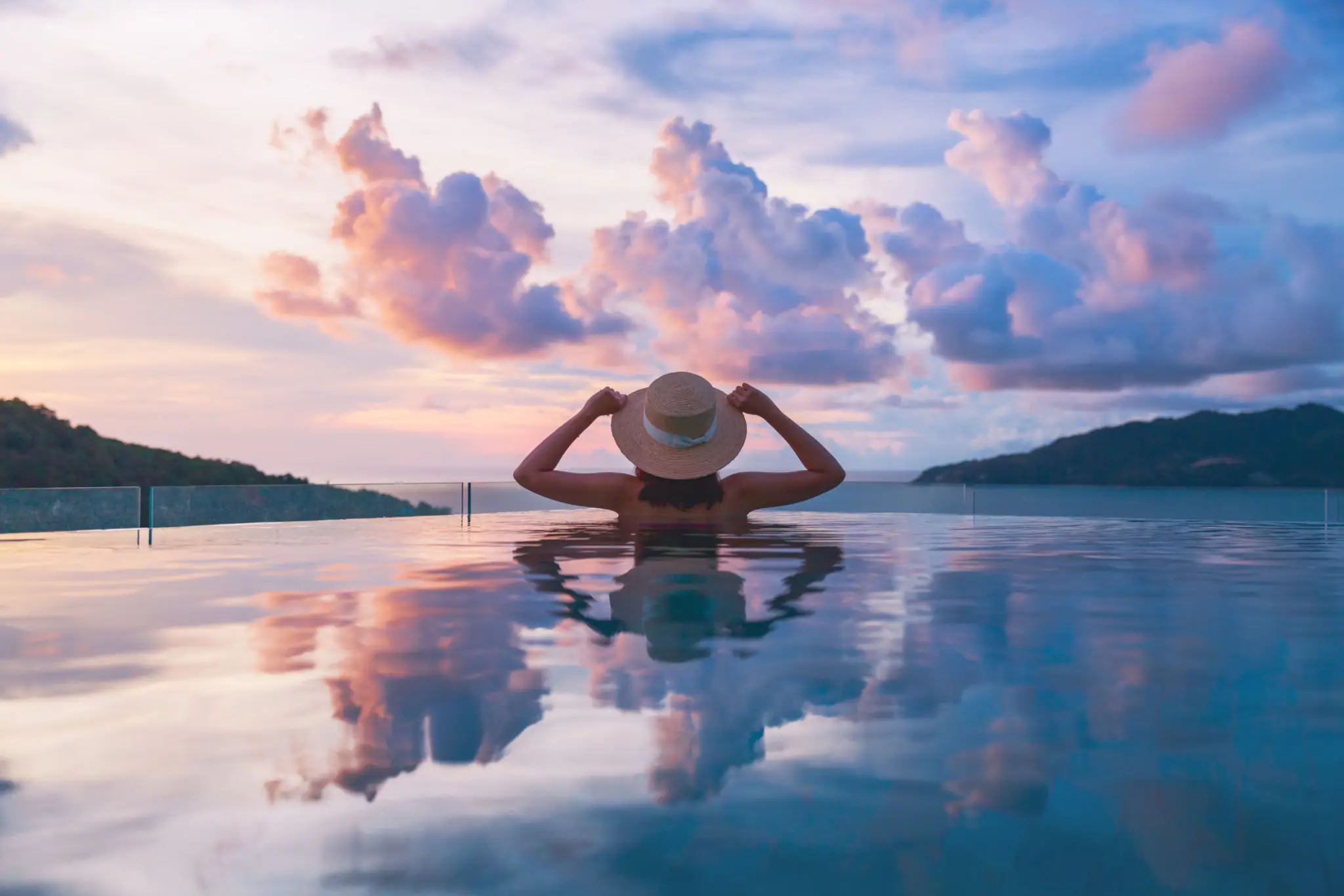 A person relaxing in a pool at sunset with a scenic view.