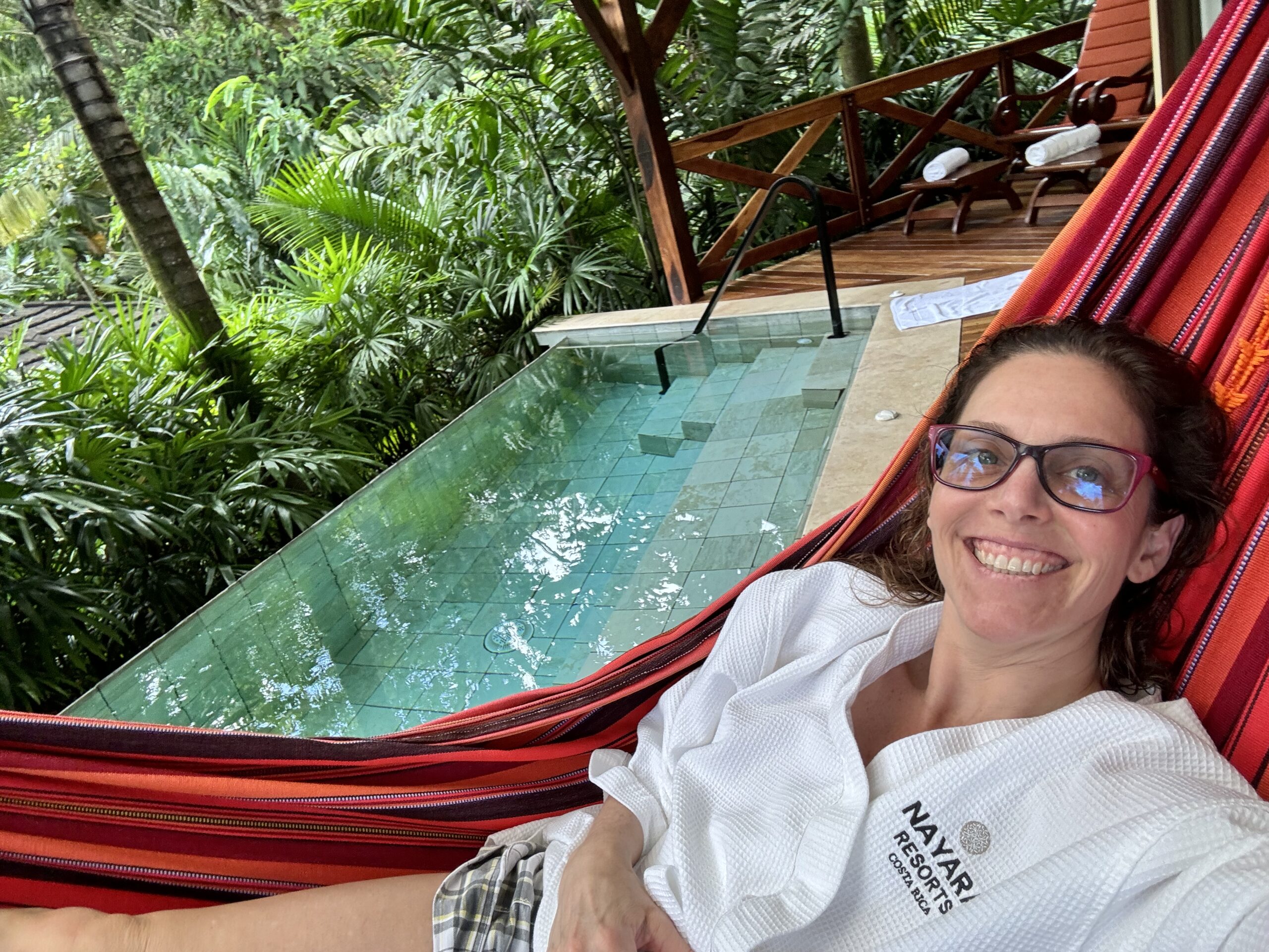 Woman relaxing in a hammock beside a serene private pool in a lush tropical setting.