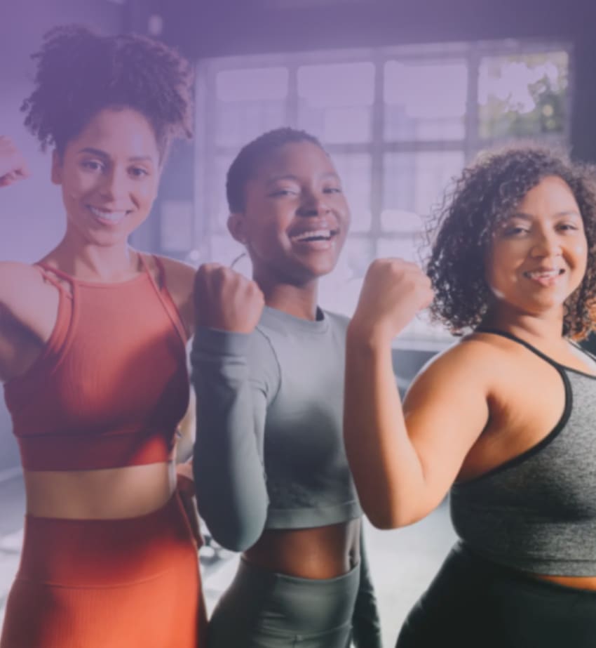 Three women smiling and showing strength in workout attire.