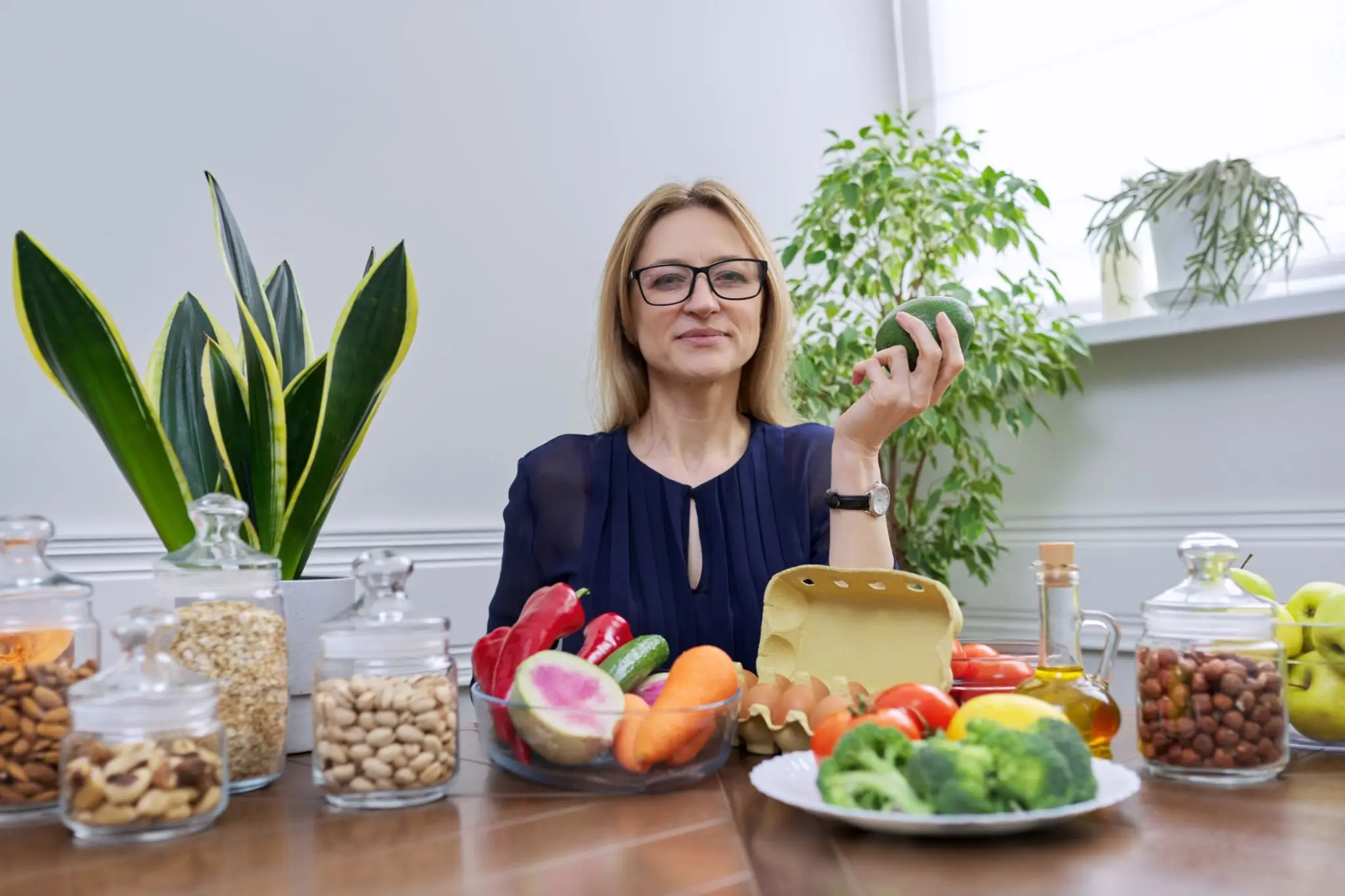 Woman holding a green apple surrounded by healthy foods and plants.