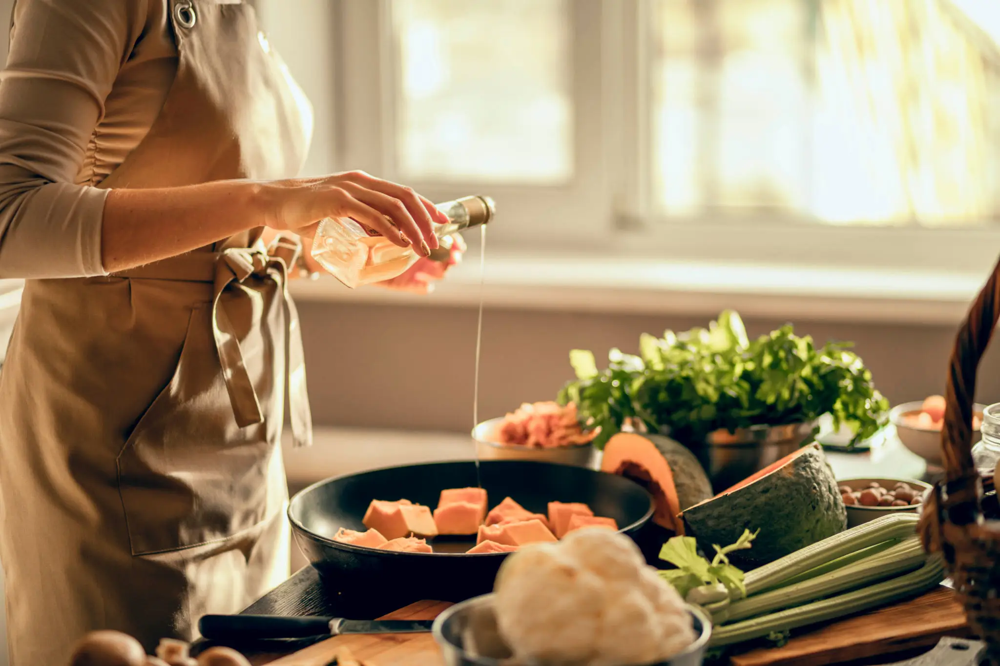 Person pouring oil into a pan with salmon and vegetables nearby.