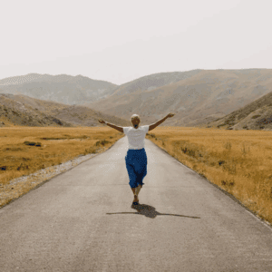 A person joyfully walks down an empty road surrounded by hills.