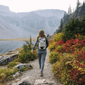 A woman hiking on a mountain trail surrounded by colorful foliage.