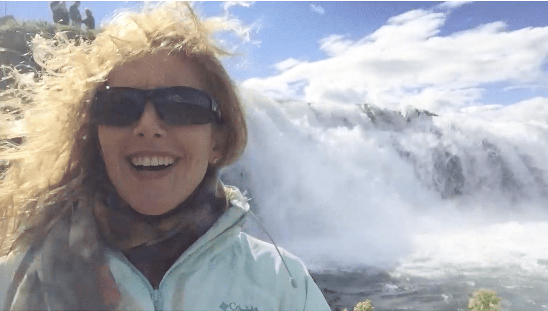 Woman visiting a dramatic Iceland waterfall surrounded by mist and rugged landscape