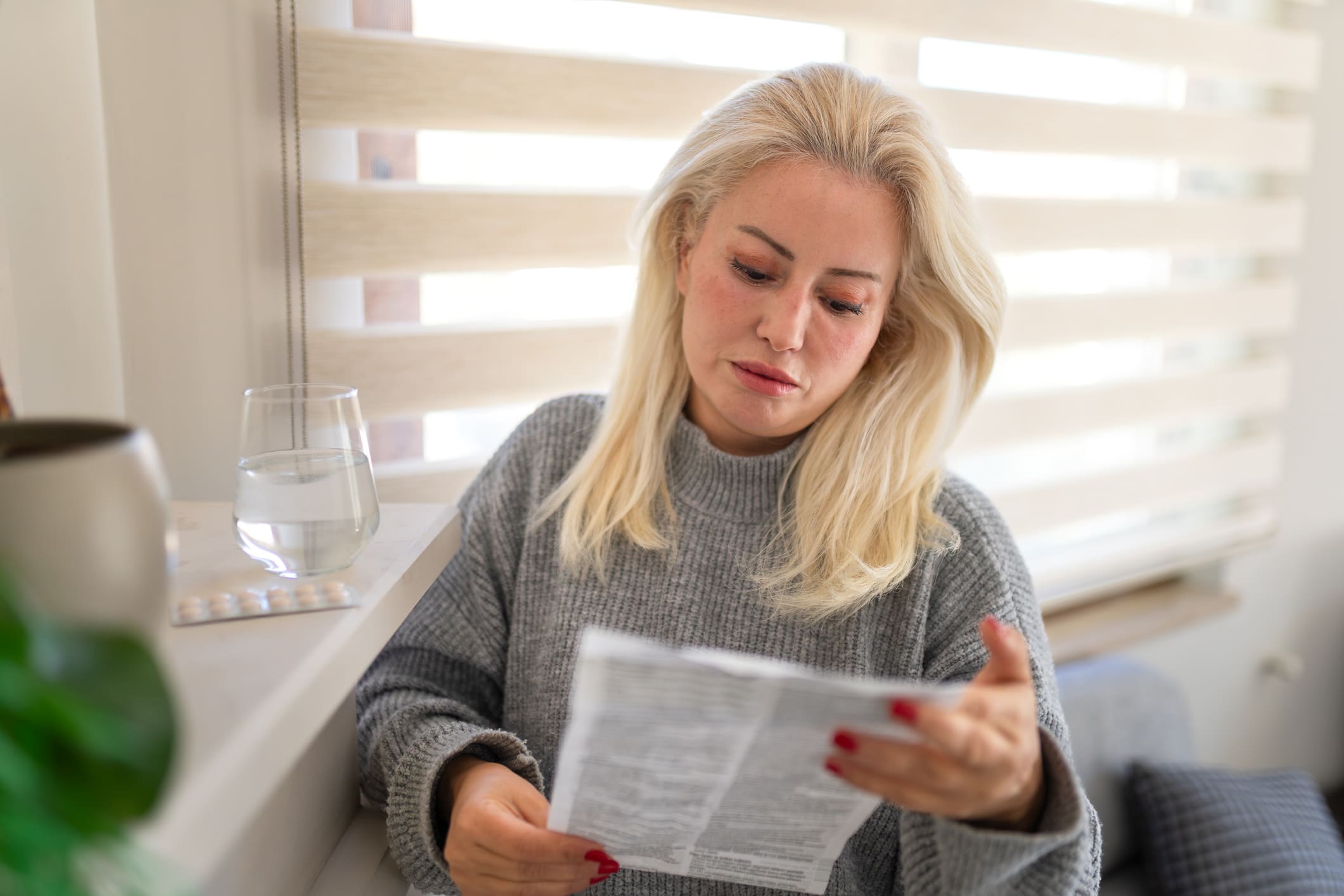 Middle aged woman reading a medication leaflet while holding pills at home. Concept of menopause management, healthcare, treatment, and understanding prescription instructions in a domestic setting