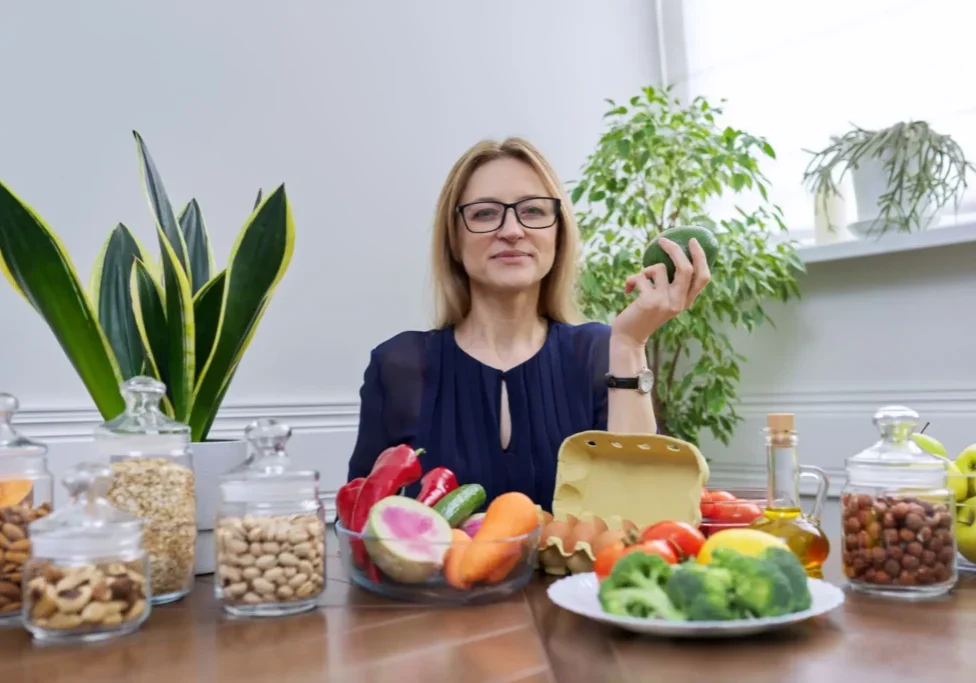 Woman holding a green apple surrounded by healthy foods and plants.