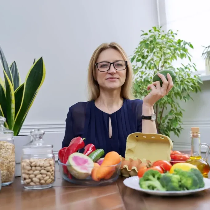 Woman holding a green apple surrounded by healthy foods and plants.