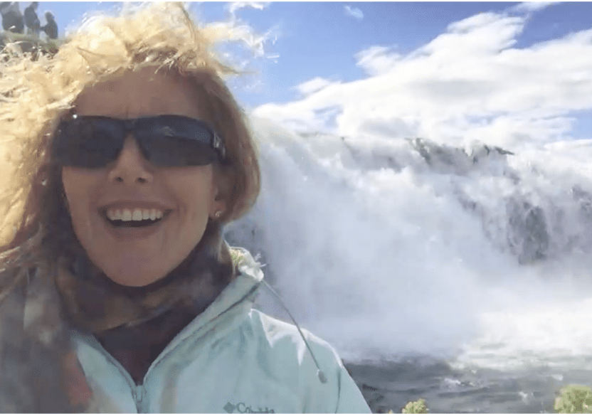 Woman visiting a dramatic Iceland waterfall surrounded by mist and rugged landscape