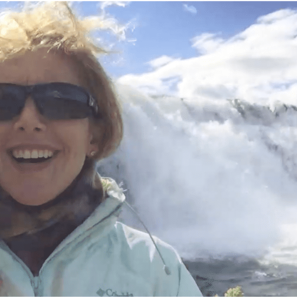 Woman visiting a dramatic Iceland waterfall surrounded by mist and rugged landscape