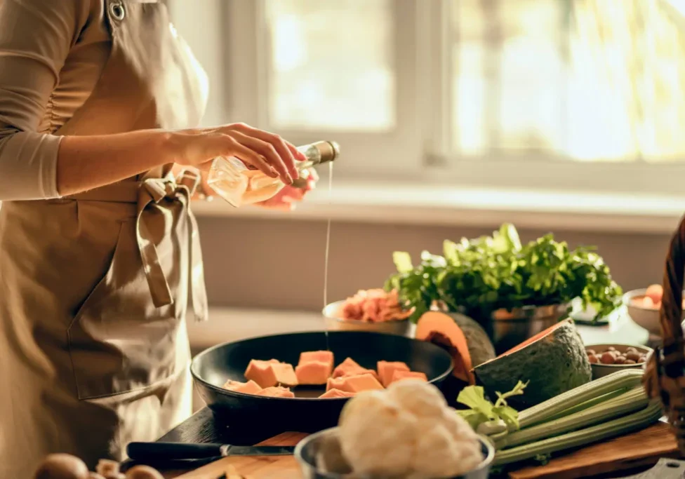 Person pouring oil into a pan with salmon and vegetables nearby.