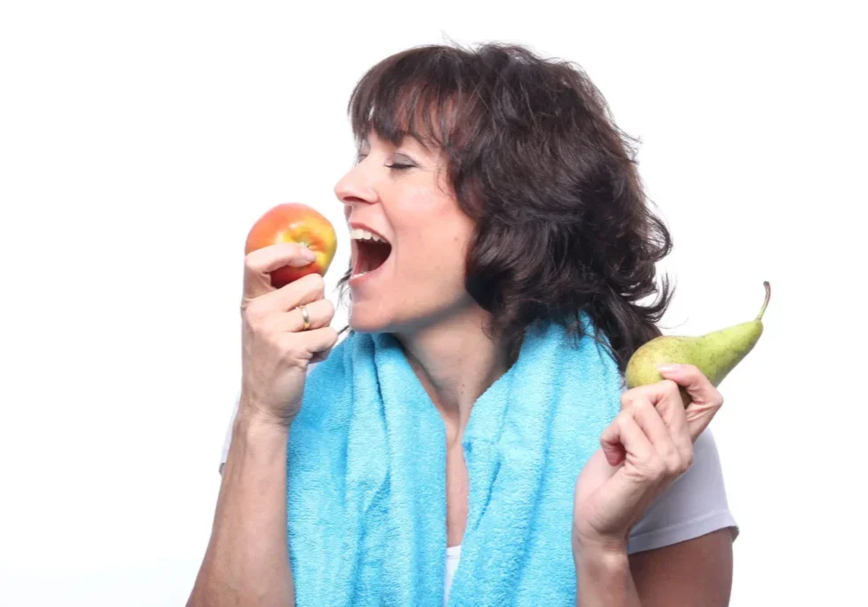Woman choosing between an apple and a pear with a towel around her neck.