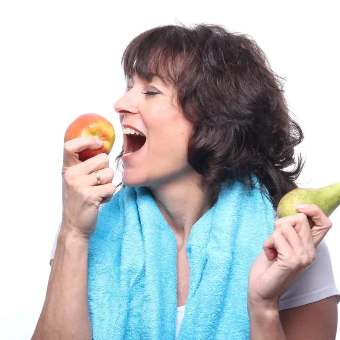 Woman choosing between an apple and a pear with a towel around her neck.
