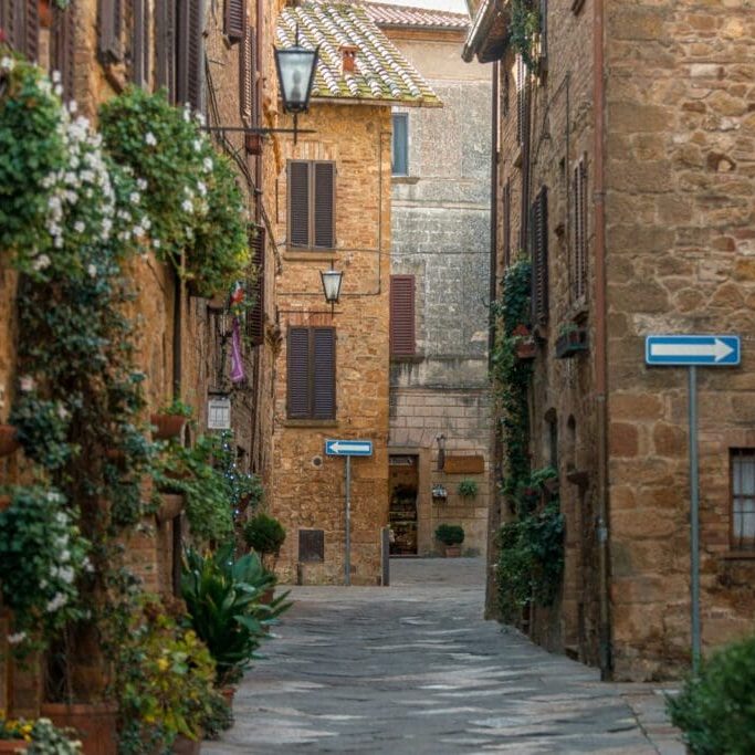 A quiet stone lane in an Italian hill town, lined with potted plants and shuttered windows
